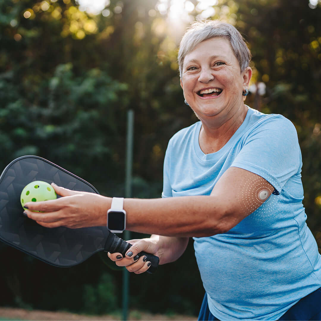 Active woman playing pickleball with LinX Vista Continuous Glucose Monitoring Sensor on her arm, showcasing health monitoring in sports.